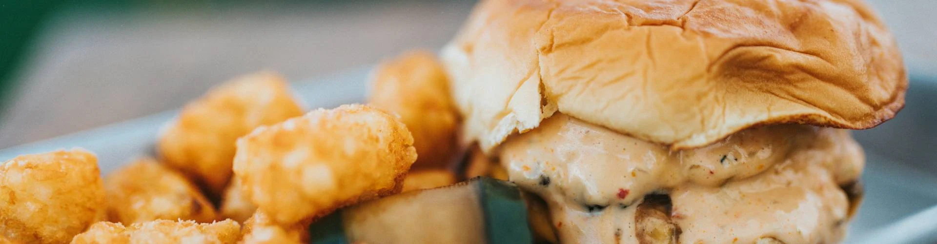 Saucy burger with some tater tots as its side dish