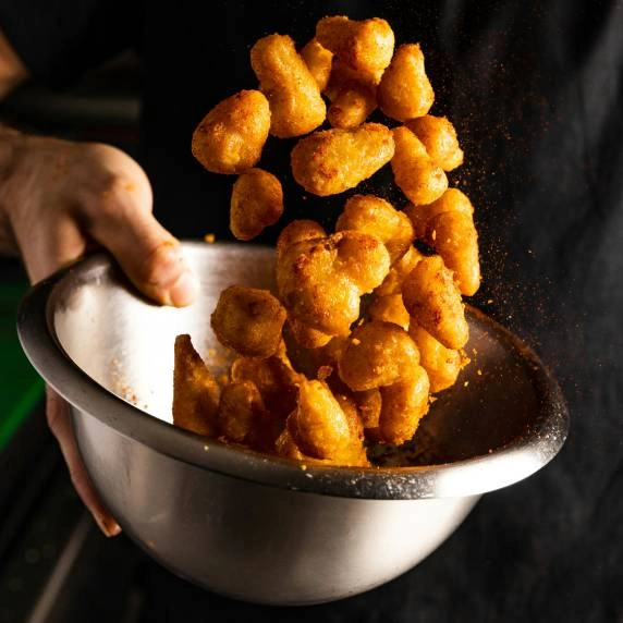 Crispy tater tots being tossed in the air by a chef